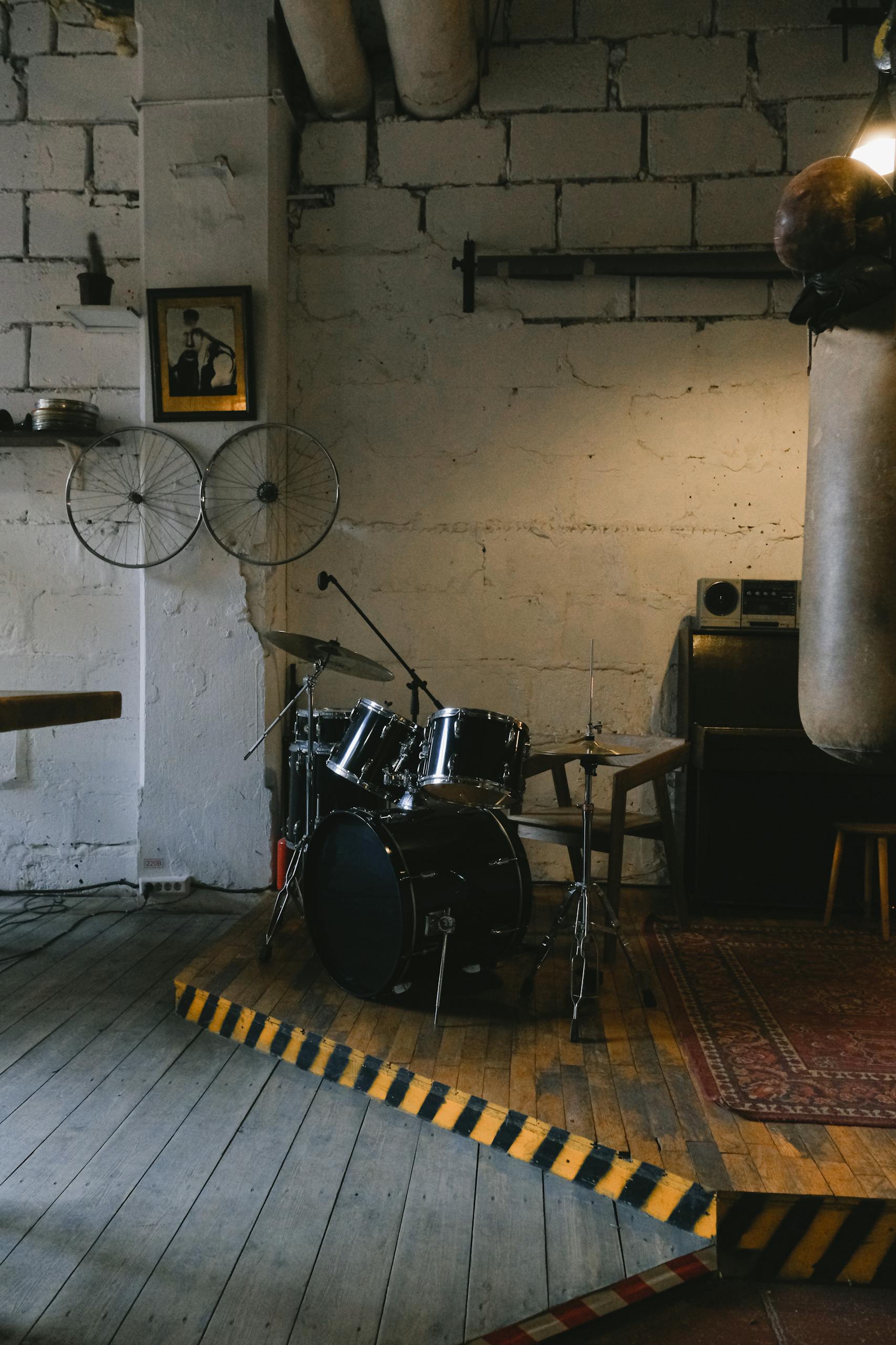 Modern drum set placed on wooden floor in contemporary studio with decorations and shelves on white shabby stone wall with lamp